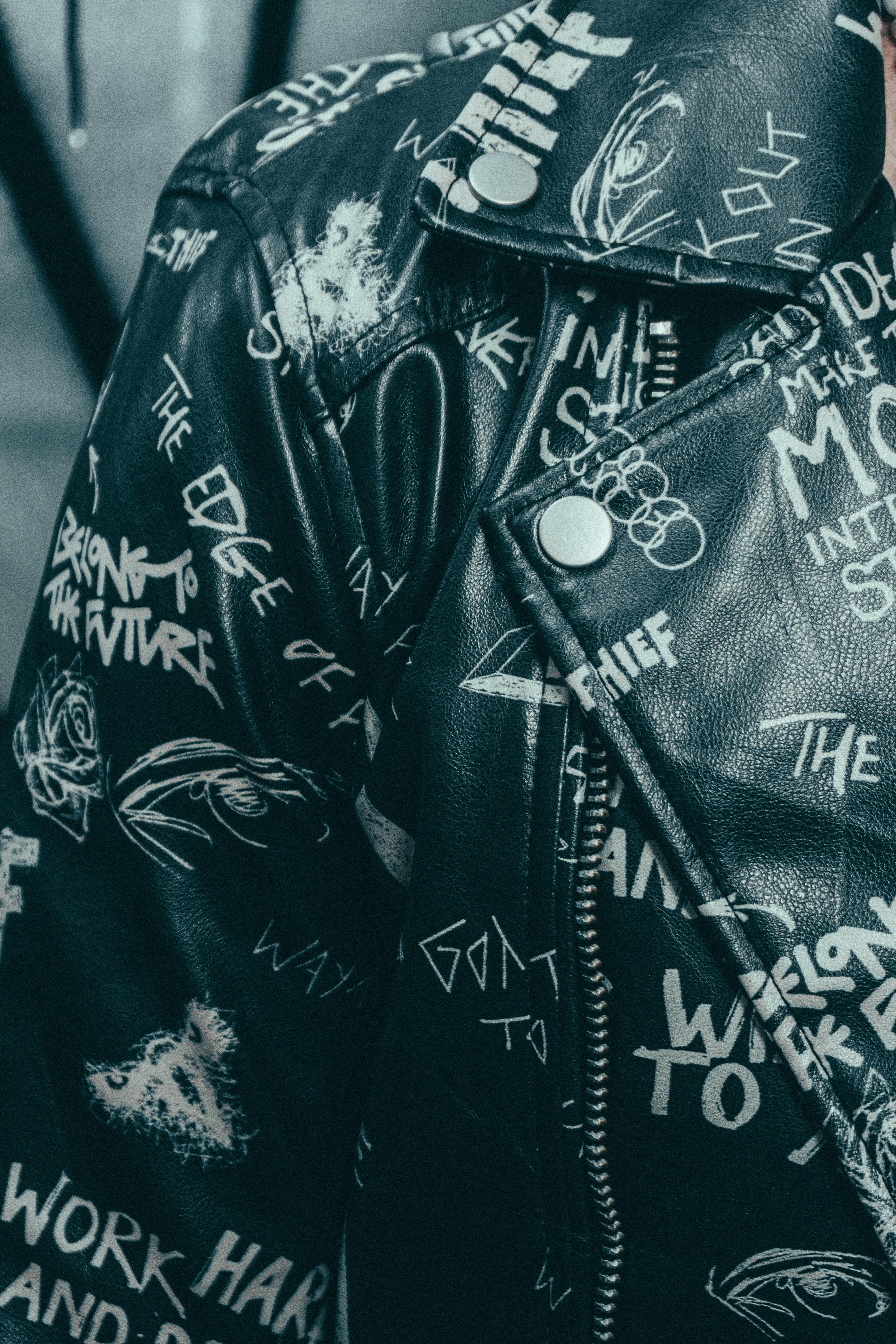 Free Close-up of a stylish black leather jacket featuring bold graffiti-style text and graphics. Stock Photo