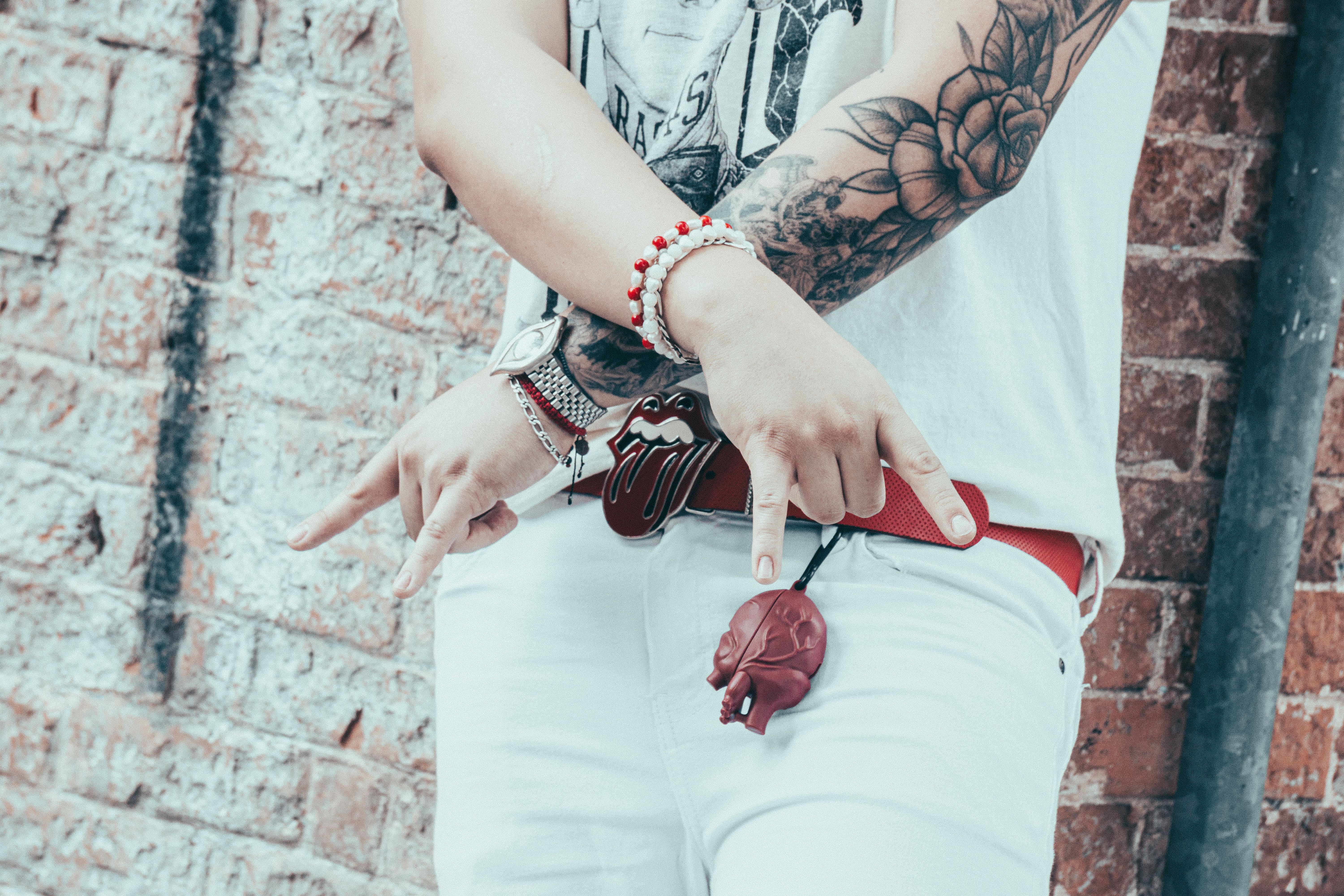 Stylish tattooed individual showcasing rock style fashion near urban brick wall.
