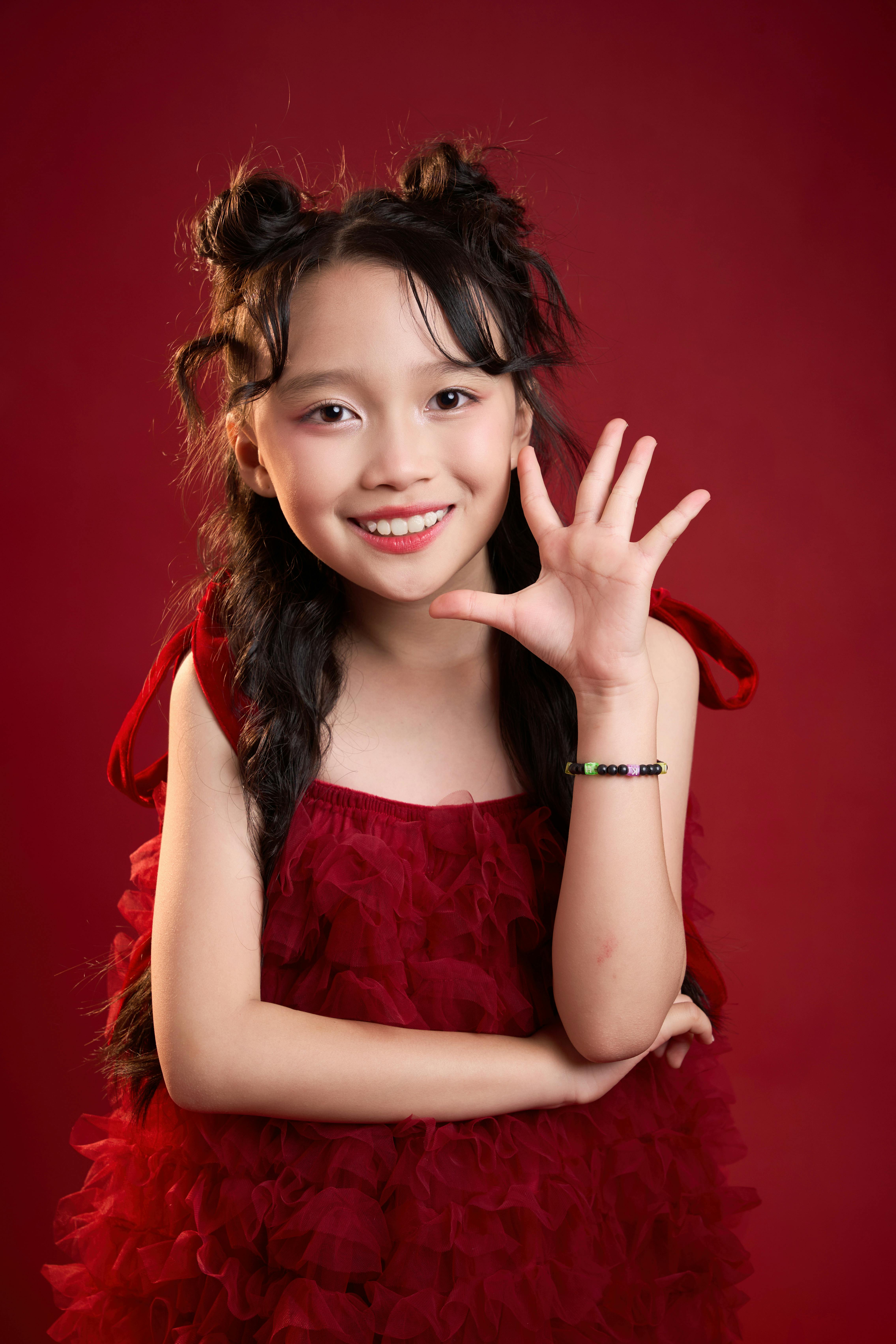 Free A joyful young girl in a red dress posing playfully in a studio setting. Stock Photo