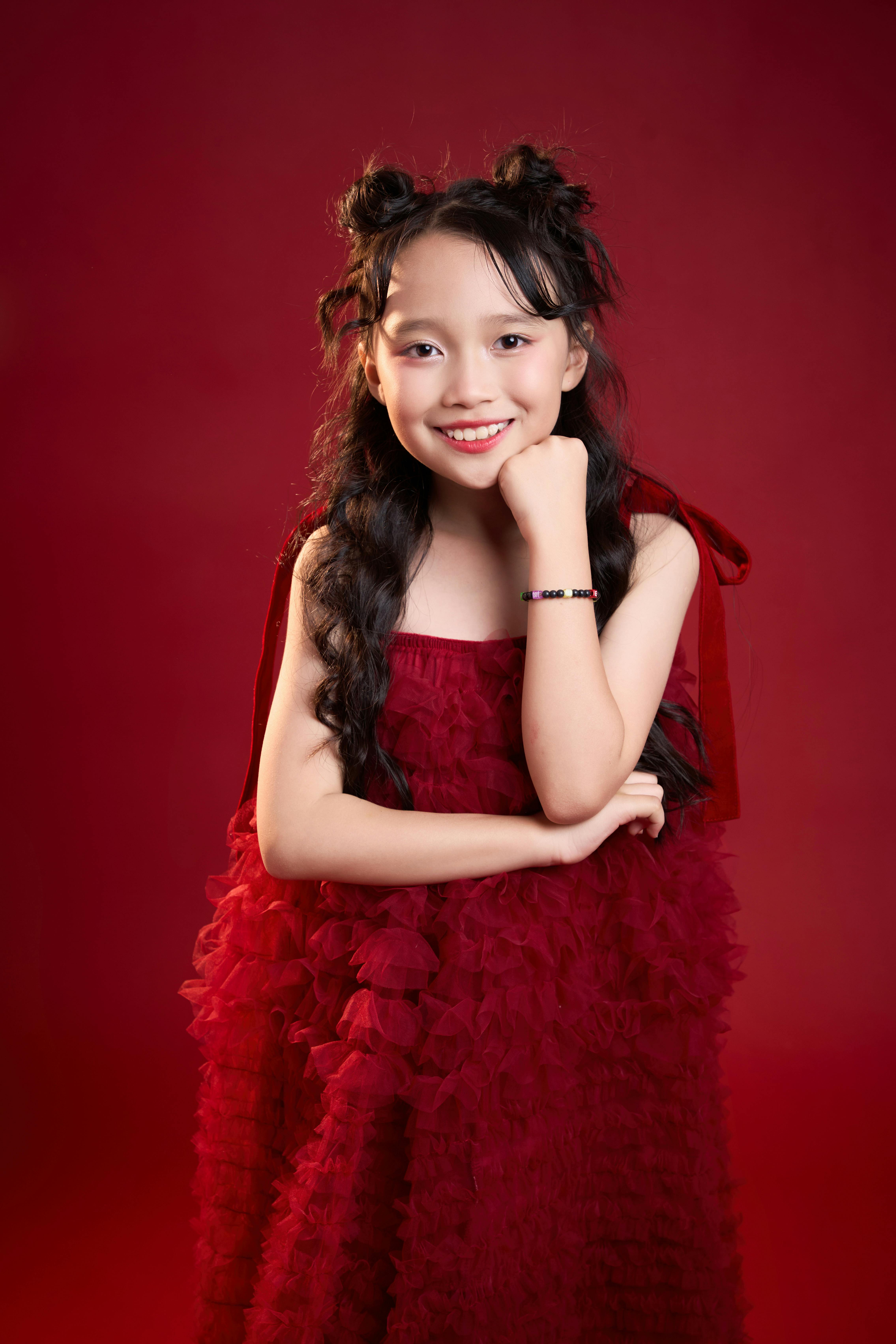 Gratis Retrato de una niña asiática sonriente con un vestido rojo sobre un fondo a juego en la ciudad de Ho Chi Minh. Foto de stock