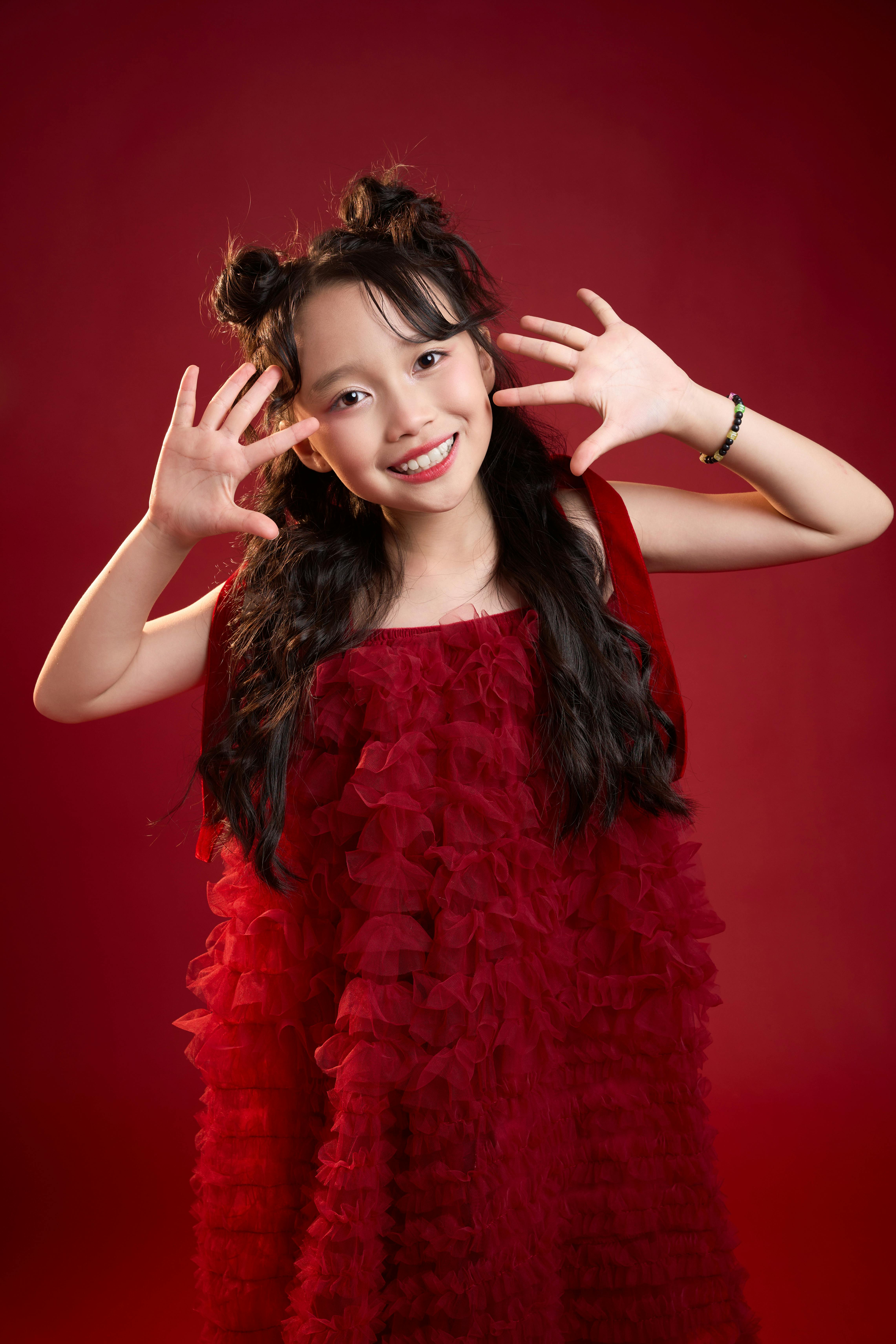 Gratis Una joven vietnamita sonríe juguetonamente con un vestido rojo vibrante en un estudio. Foto de stock