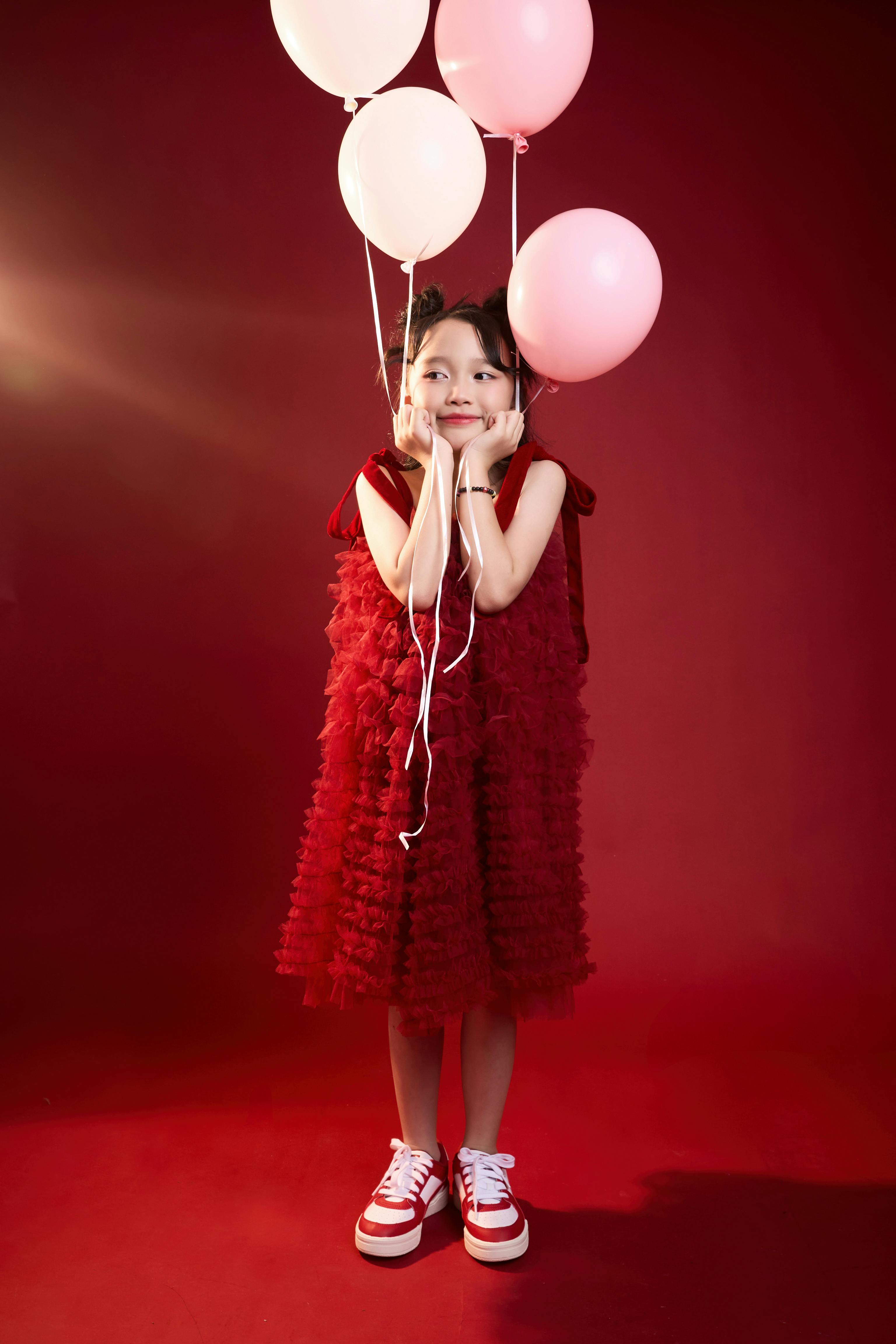 Kostnadsfria Bedårande flicka i en röd klänning som håller ballonger, mot en livlig röd bakgrund. Stock foto