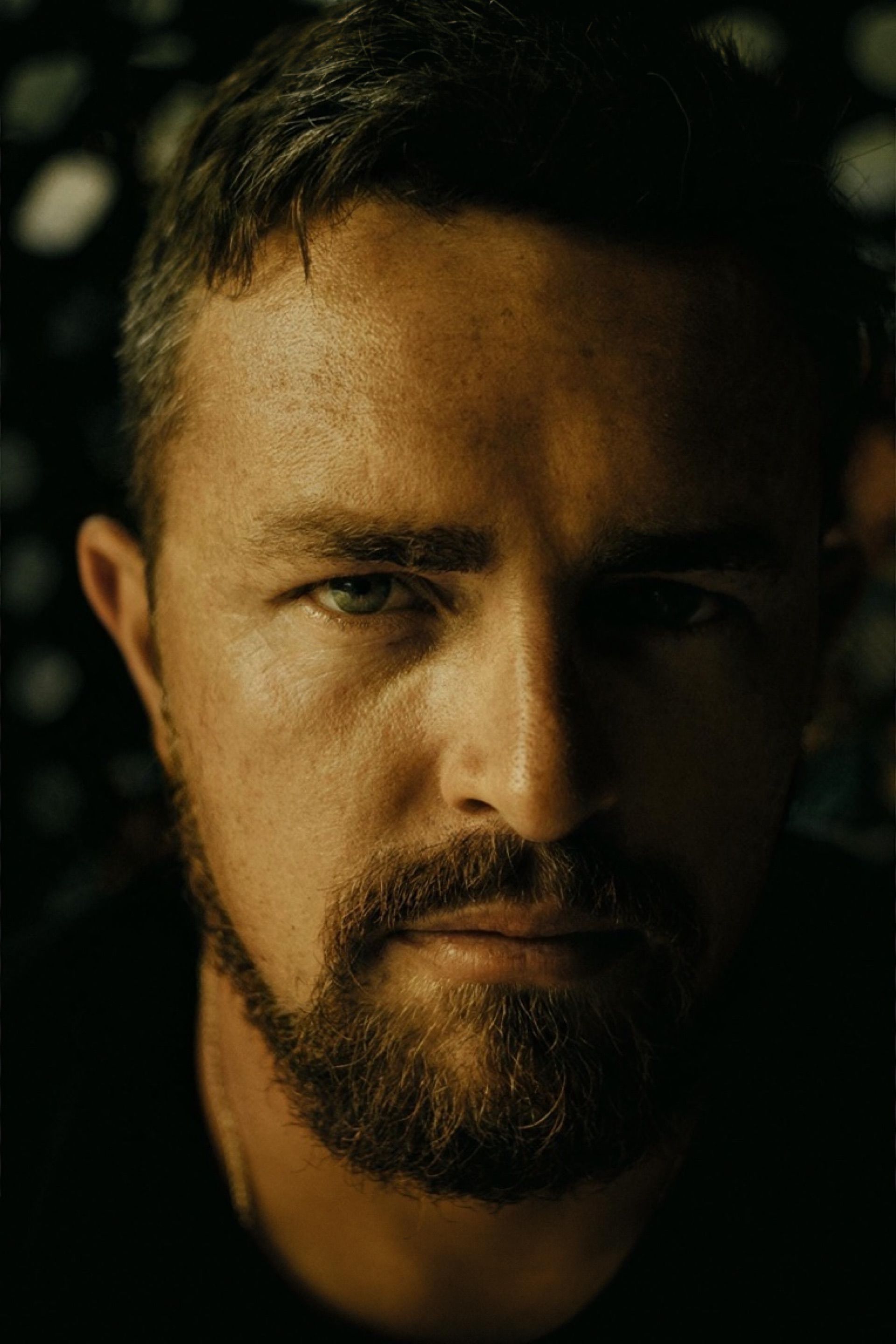 Intense close-up portrait of a serious bearded man in dim lighting.