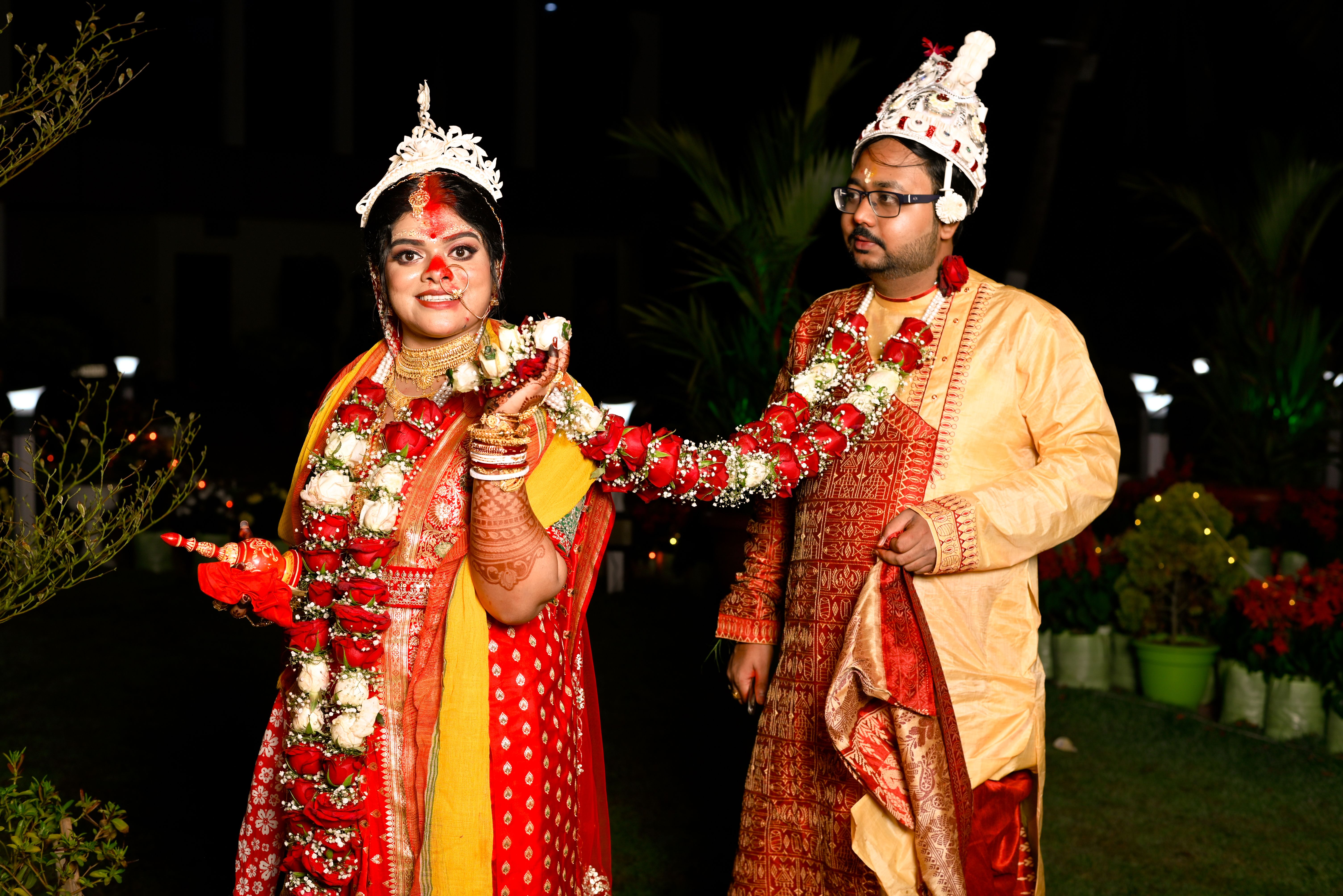 A bride and groom in traditional attire during an Indian wedding ceremony held outdoors at night.