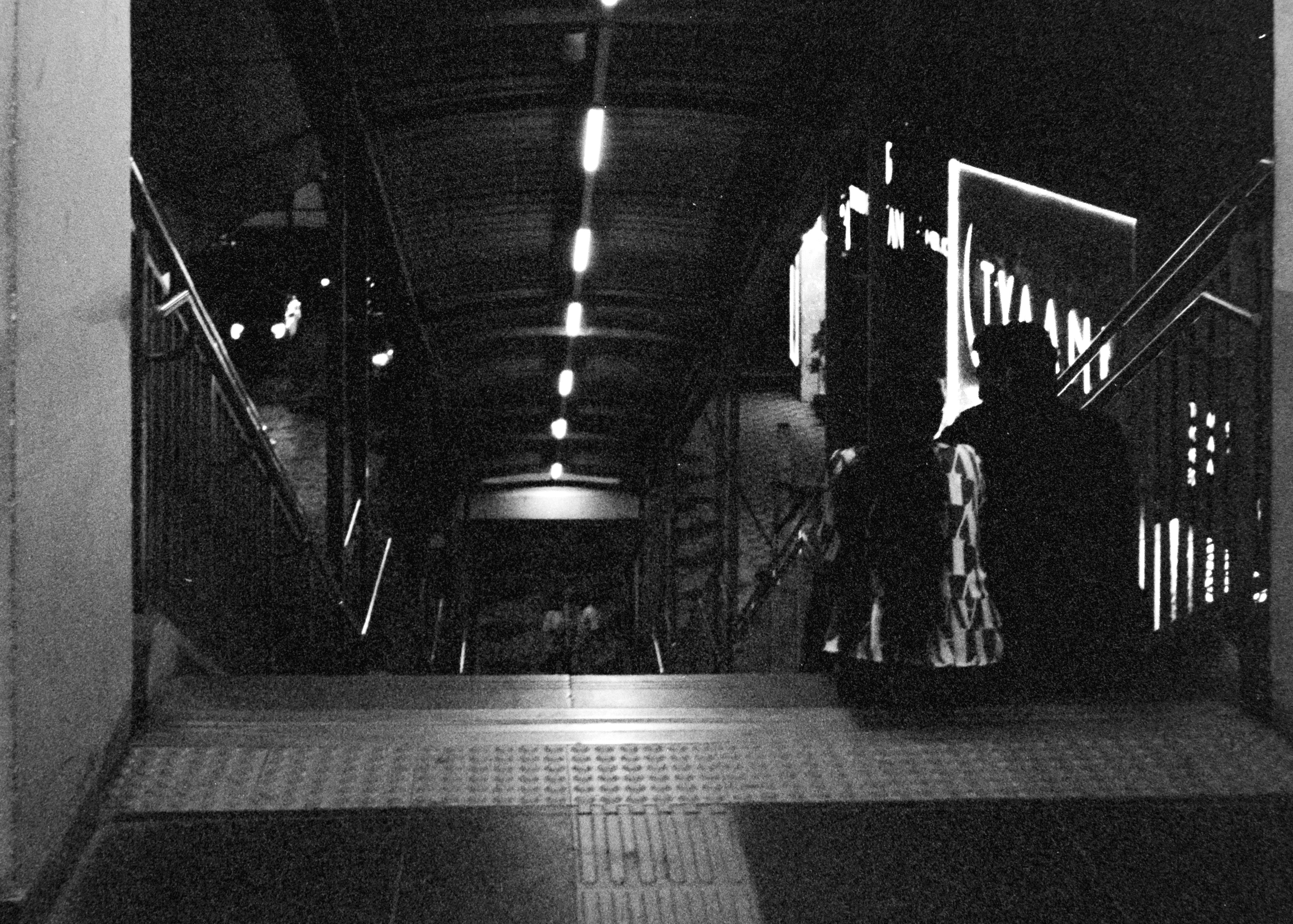 A black and white photograph capturing a nighttime urban setting with people on a staircase.