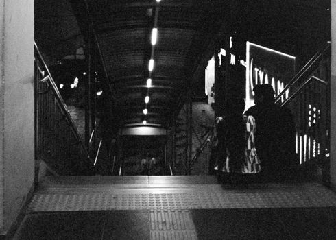 A black and white photograph capturing a nighttime urban setting with people on a staircase.