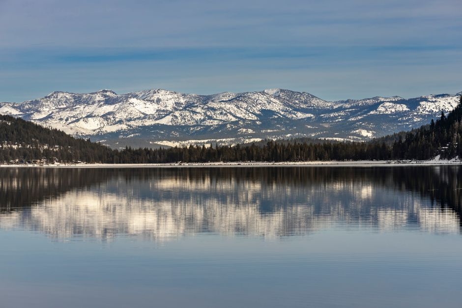 Serene winter landscape featuring snow-covered mountains reflected on Donner Lake's calm waters.