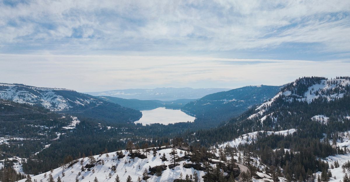 Breathtaking aerial view of Donner Lake surrounded by snow-covered mountains under a cloudy sky.
