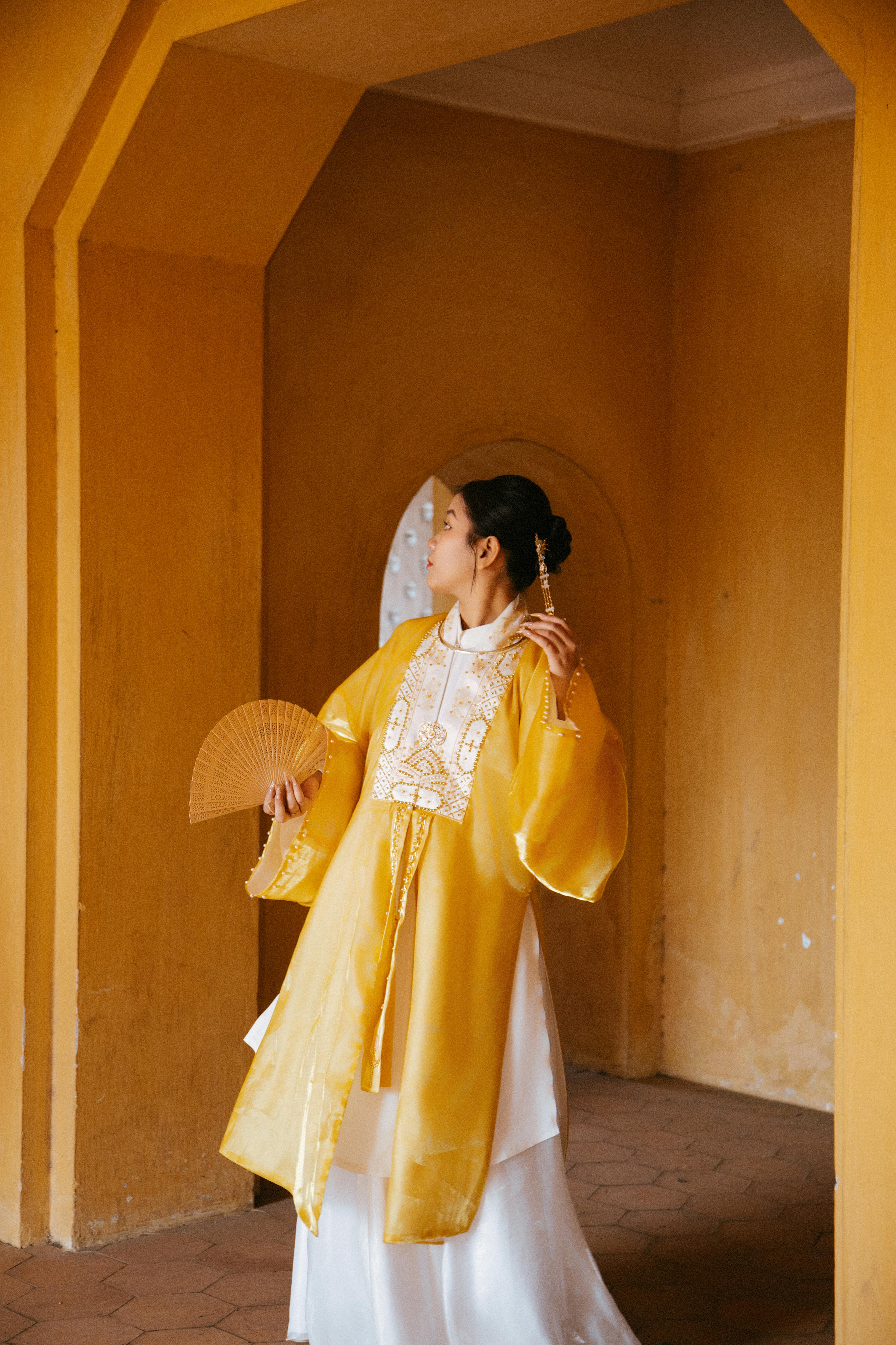 A woman in traditional Vietnamese clothing stands elegantly in an arched hallway.