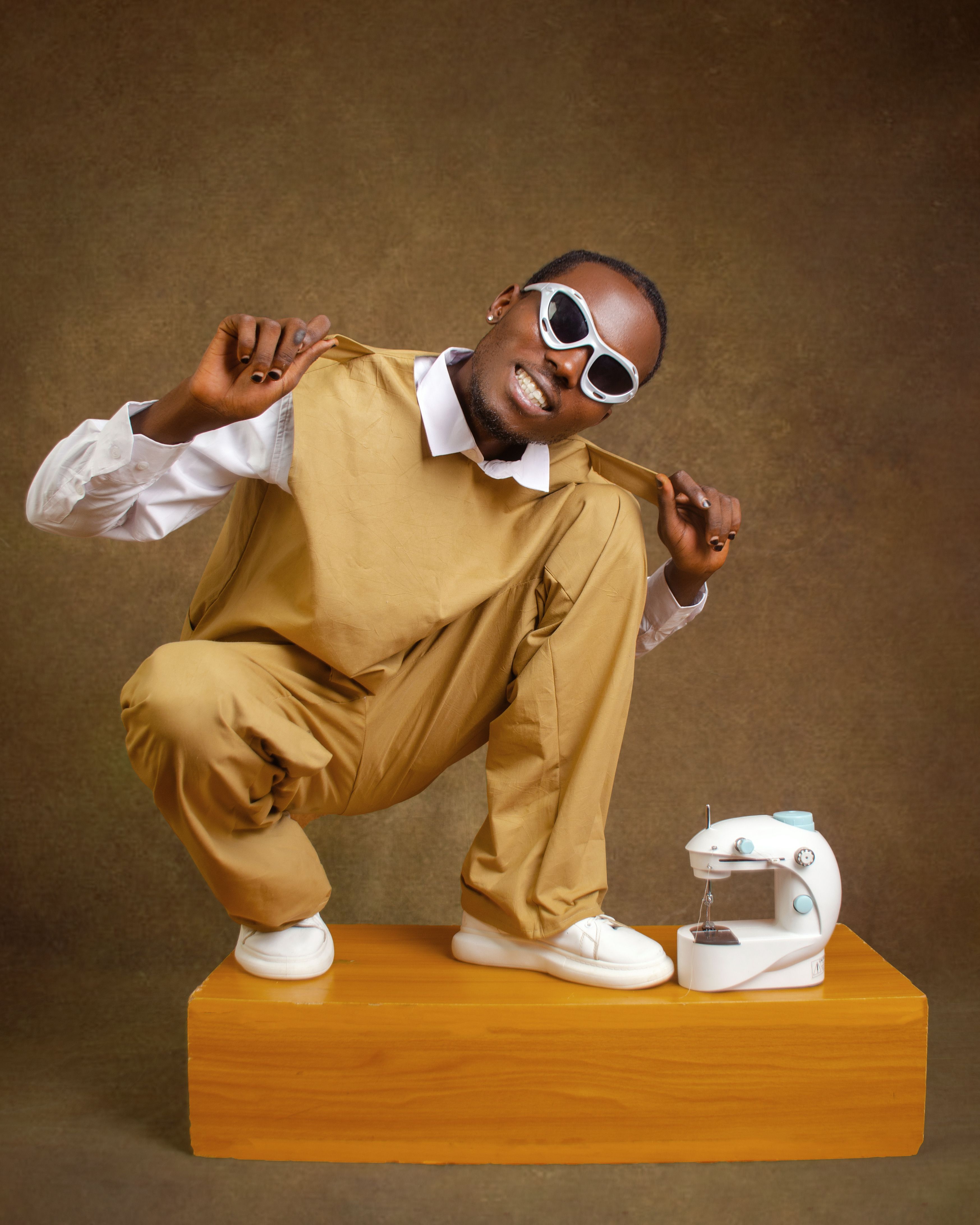 Stylish individual in sunglasses posing with sewing machine in studio setting.