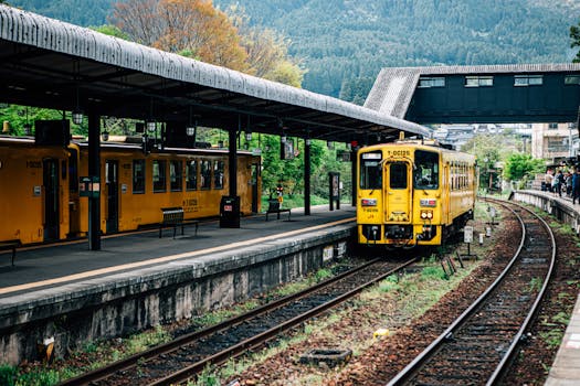 Charming yellow train at a picturesque rural railway station amid lush greenery.