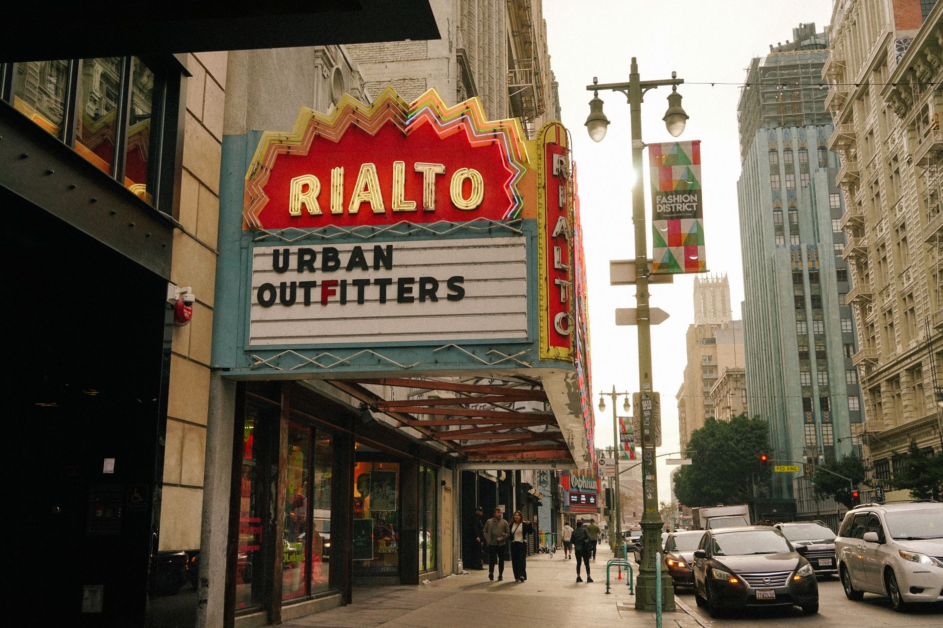 Street view of Rialto Theater sign in Los Angeles Fashion District with people and cars on a busy day.