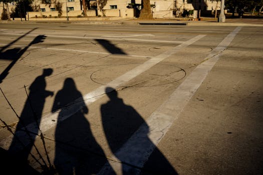 Silhouettes of three individuals create dramatic shadows on a city street crosswalk.