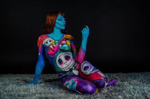 Free A woman in surreal body paint costume seated against a dark background, exuding artistic flair. Stock Photo