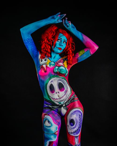 Free Model with colorful surreal body paint poses with confidence in dark studio backdrop. Stock Photo