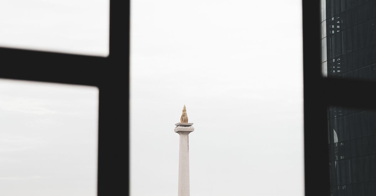 View of the National Monument in Jakarta framed by windows, showcasing Indonesia's iconic landmark.