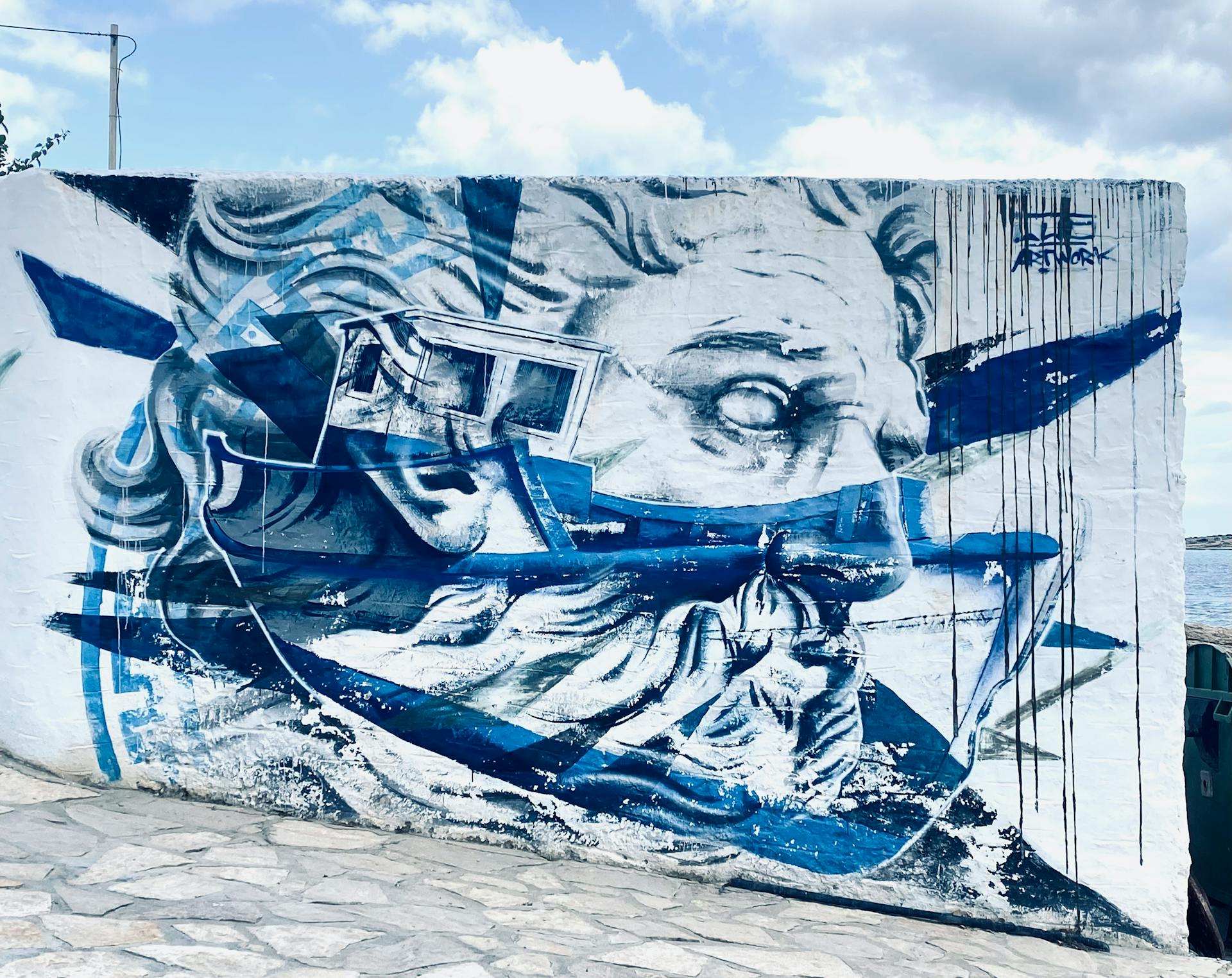 Colorful street art depicting Greek mythology on a white island wall, creating a vivid coastal scene.