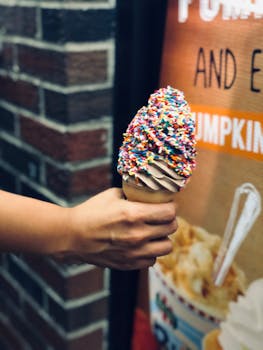 A close-up view of a hand holding a chocolate ice cream cone with vibrant sprinkles.
