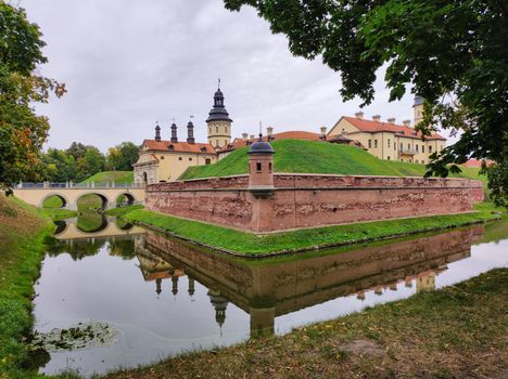 Scenic view of the historic Nesvizh Castle reflecting in water on a cloudy day.