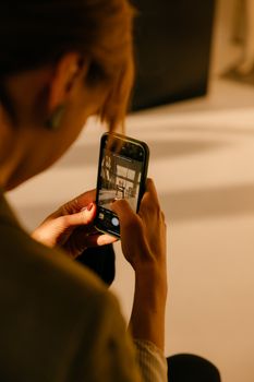 A woman photographing an interior setting with her smartphone, focused and engaged.