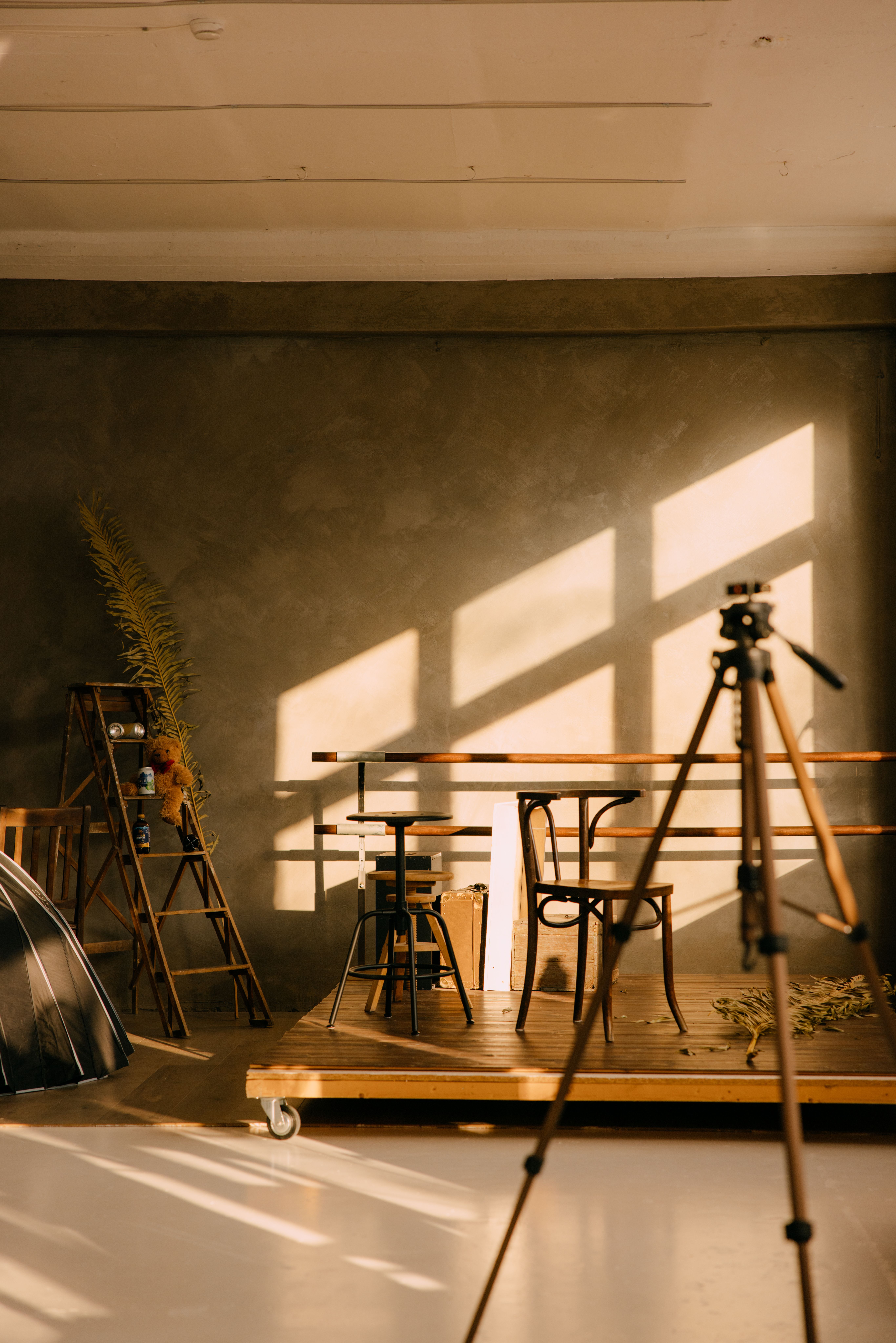 Warmly lit photography studio with rustic decor, tripod, and shadows casting on walls.