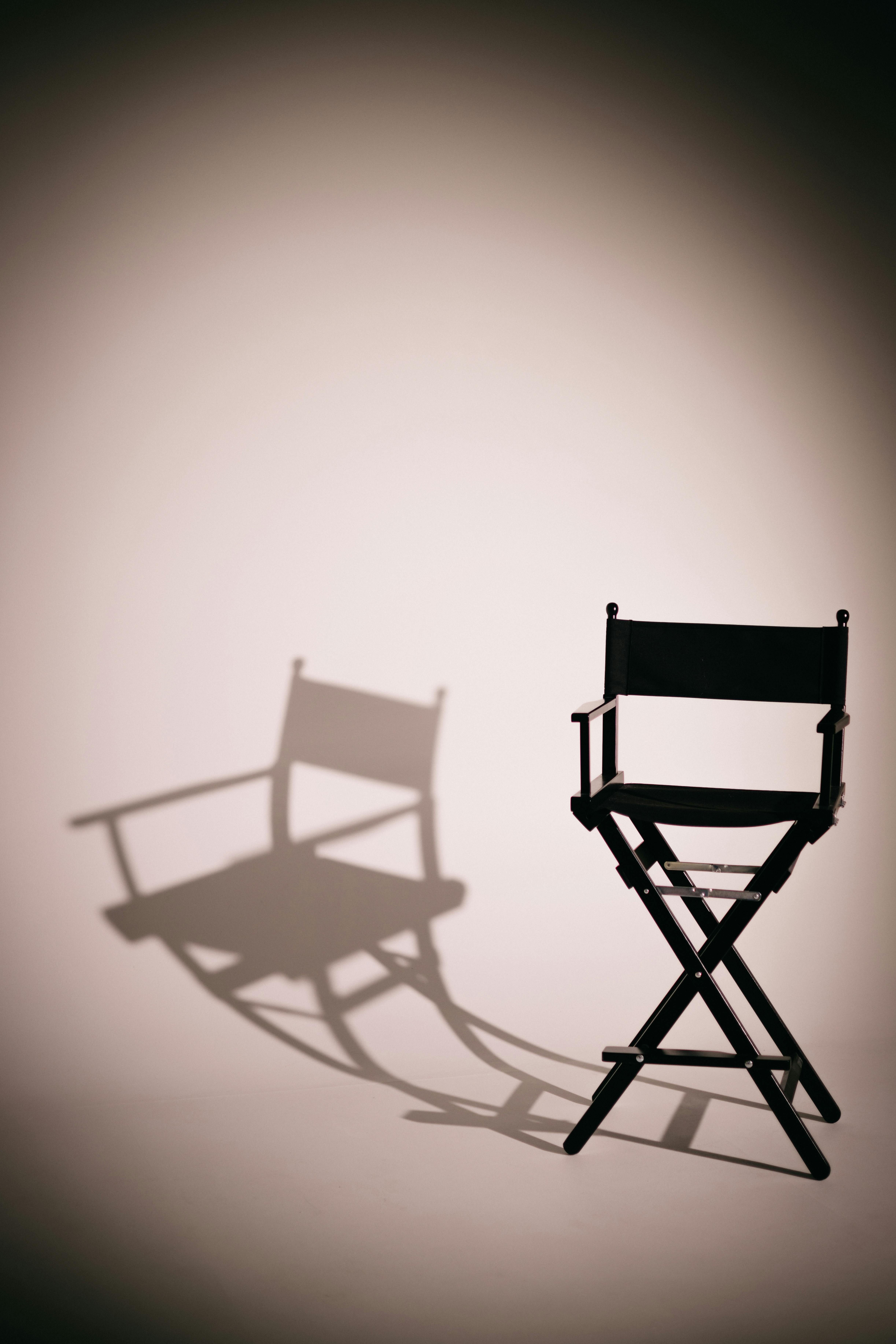 Free Director's chair casting an artistic shadow in a minimalist studio setting, perfect for creative design. Stock Photo