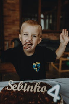 A cheerful child enjoying their fourth birthday with a chocolate cake indoors.