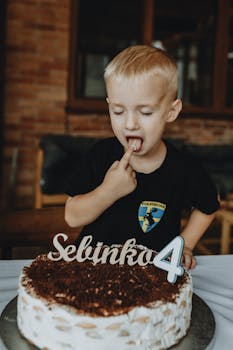 Blond child enjoying a birthday cake with '4' decoration indoors, celebrating a special day.