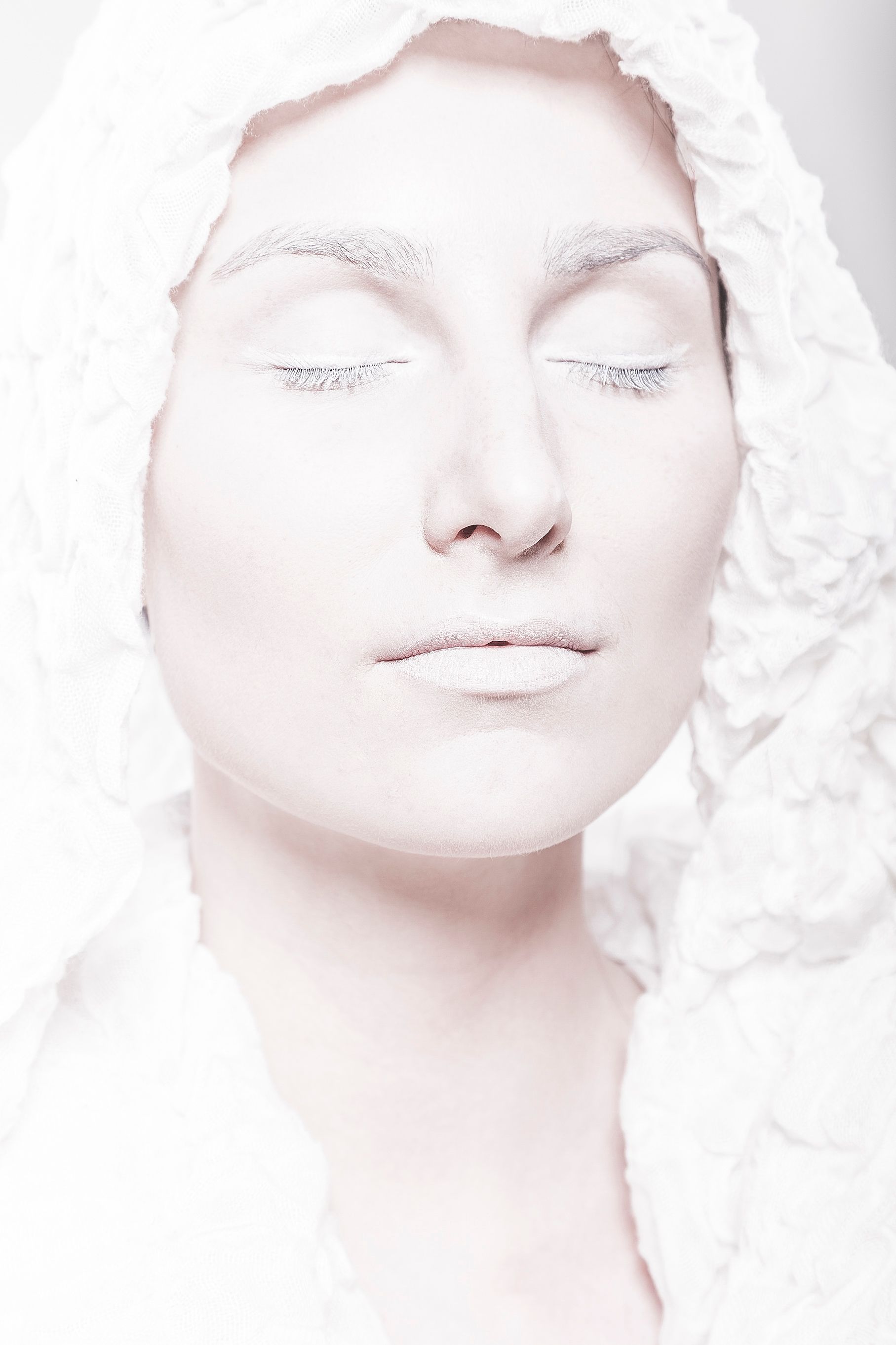 A serene and artistic portrait of a woman with eyes closed, enveloped in white fabric, exuding tranquility.