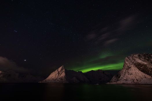 Spectacular view of the Northern Lights illuminating snowy peaks under a starlit sky.