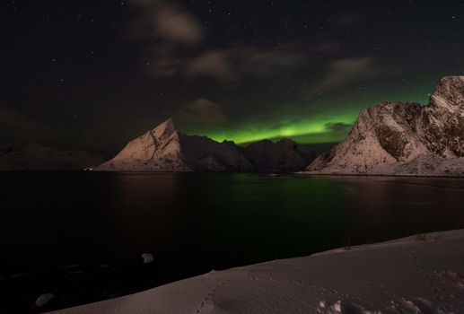 Scenic view of Aurora Borealis over snowy mountains and fjords in Norway at night.