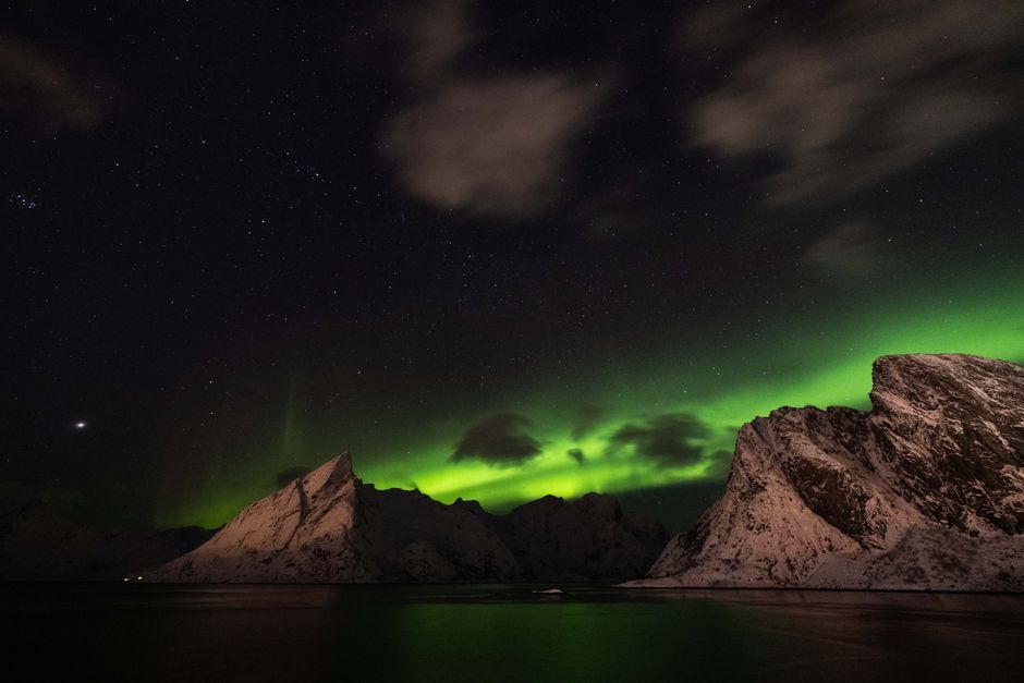 Breathtaking view of the Northern Lights above snow-covered mountains and a starry sky.