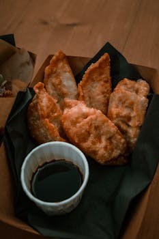 Crispy gyoza served in a box with a savory dipping sauce, perfect for street food lovers.