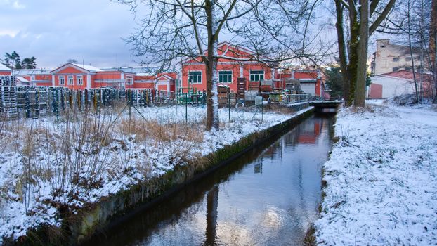 Snow-covered canal beside industrial buildings in winter landscape.