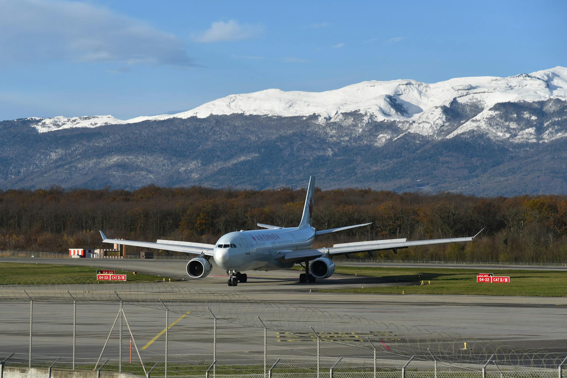 Commercial aircraft taxiing on the runway at Geneva Airport with a mountain backdrop.