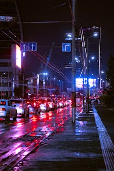 City street at night with cars, neon lights, and wet reflections reflecting urban nightlife.