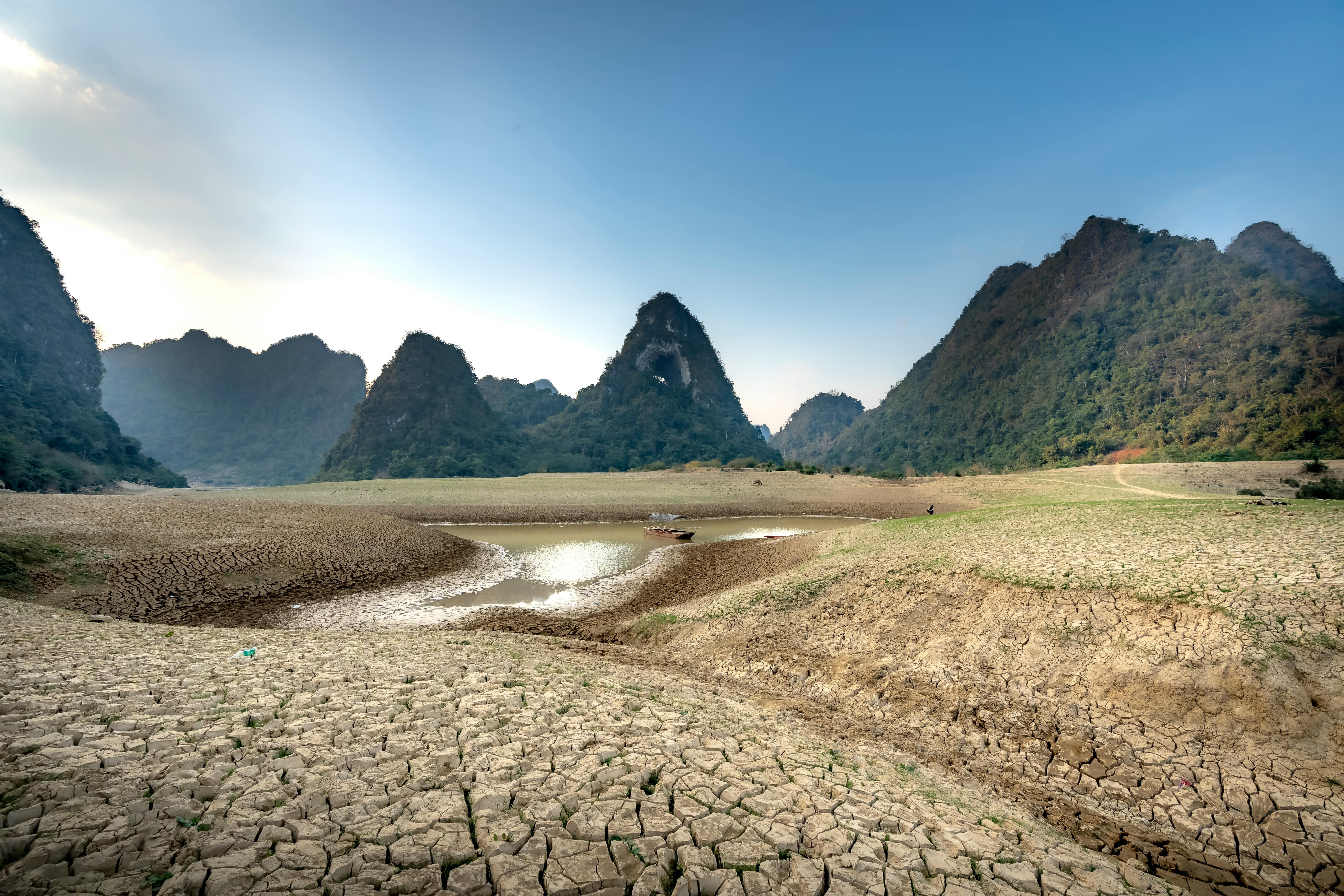 Dramatic dry landscape with cracked earth, sparse water, and striking mountains under a blue sky.