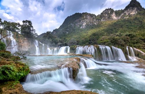 Free Stunning view of cascading waterfalls amid lush mountains under a blue sky. Stock Photo