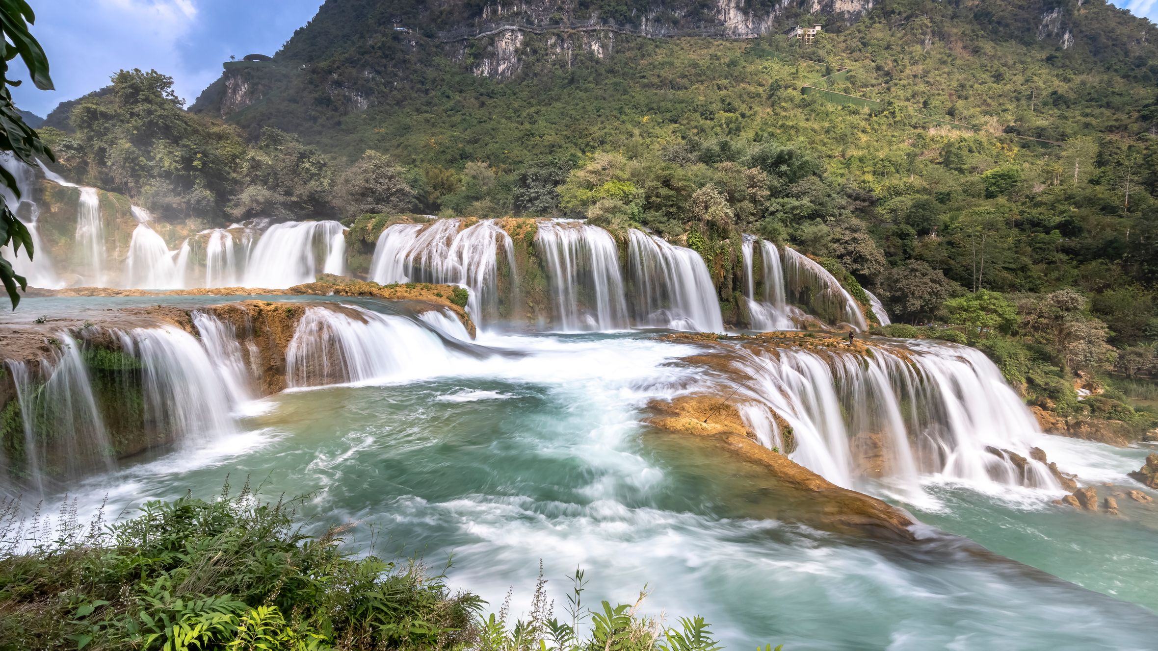 Breathtaking view of a cascading waterfall surrounded by lush greenery and mountains.