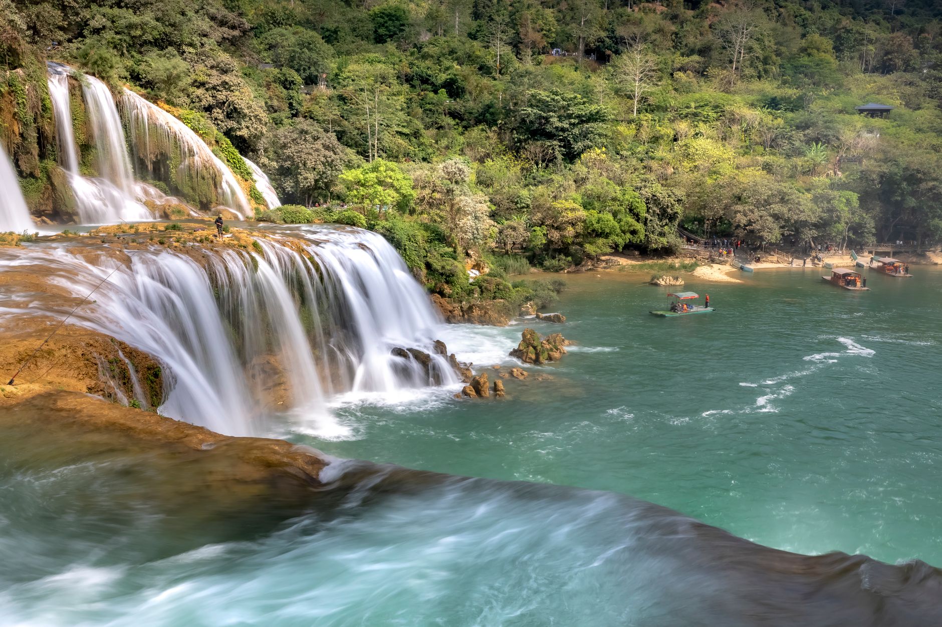 Serene waterfall flowing into a clear turquoise river surrounded by lush greenery and rocky cliffs.
