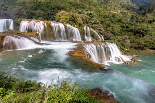 Free A stunning view of a large waterfall flowing through a dense green forest landscape. Stock Photo