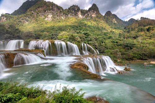 Free Scenic waterfall cascading in a vibrant green mountain landscape, perfect for nature lovers. Stock Photo