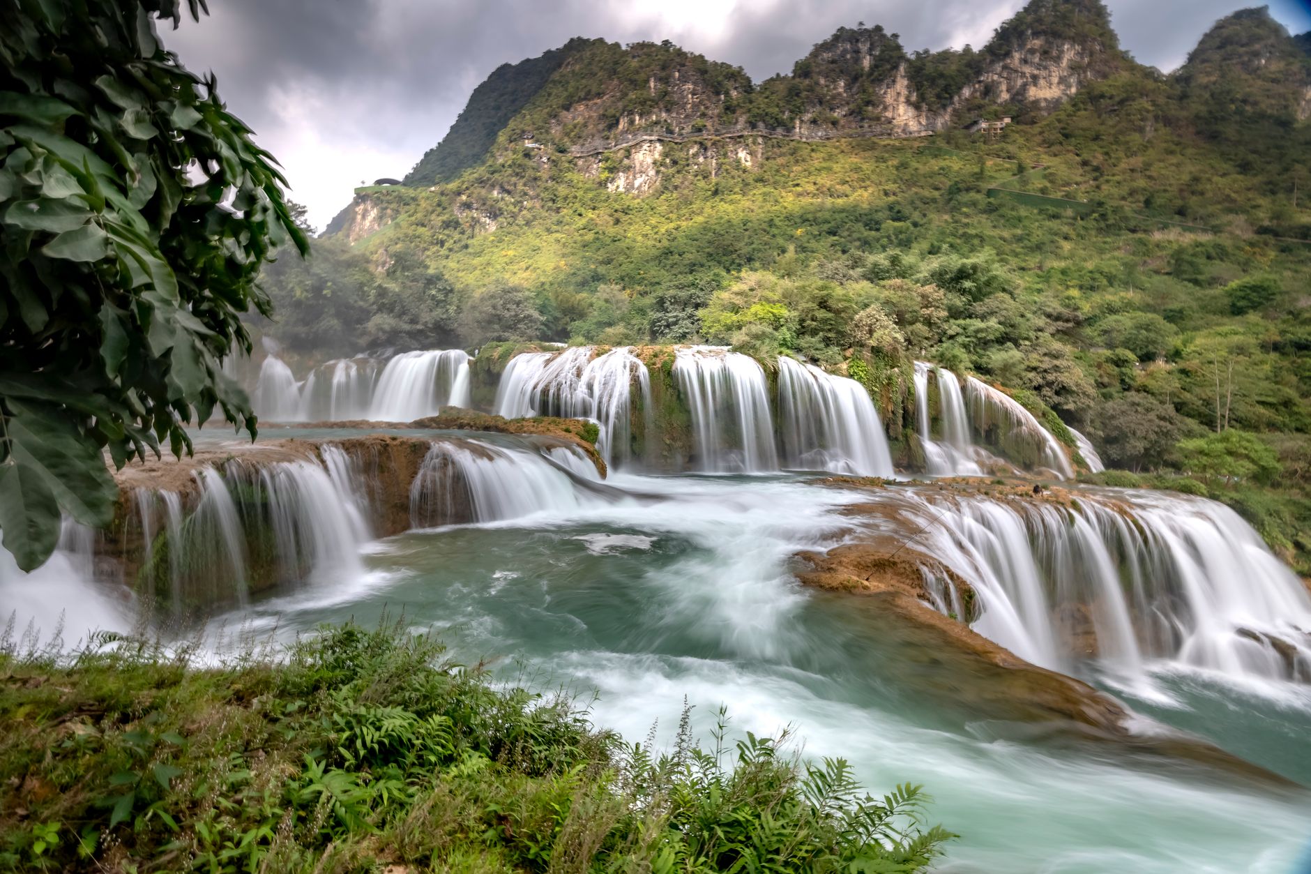Scenic view of the Ban Gioc Waterfall surrounded by lush greenery and rocky mountains.