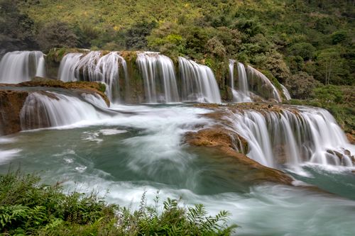 Free Breathtaking view of cascading waterfall surrounded by lush green forest, creating a peaceful natural scene. Stock Photo