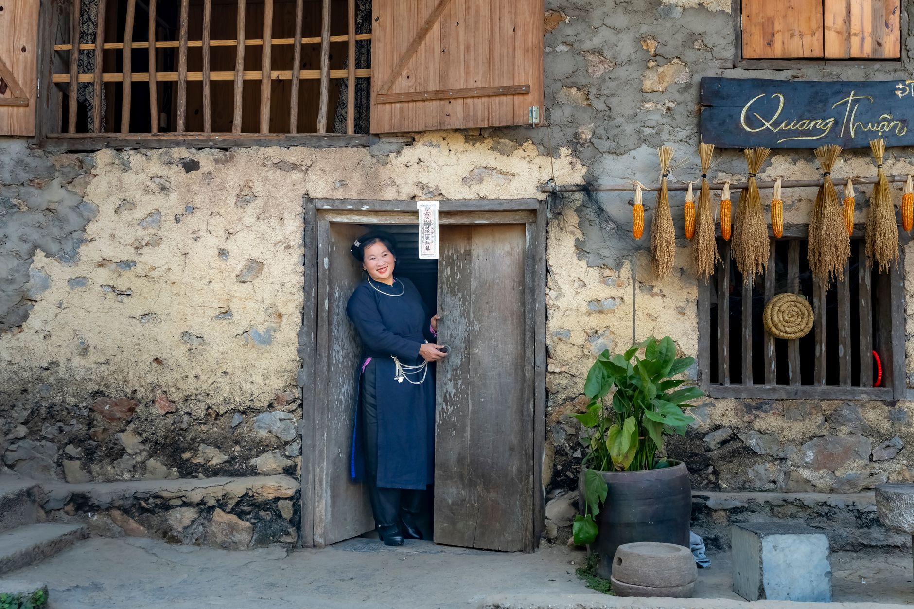 Woman in traditional attire stands in the doorway of a rustic Vietnamese house.