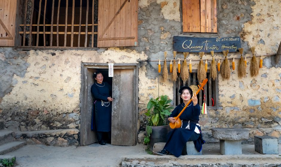 Sustainable community tourism model in Quang Ninh, Vietnam, showing local hosts welcoming visitors at a simple eco-friendly homestay, signage about cultural etiquette and waste sorting, green surroundings, authentic and responsible travel atmosphere, highly detailed