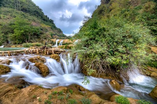 Free Majestic waterfall amidst a vibrant green valley surrounded by rocky terrain and dense foliage. Stock Photo