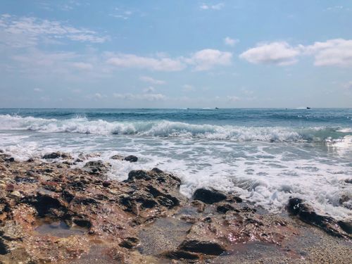 Free Tranquil ocean waves gently hit the rocky shore under a bright blue sky. Stock Photo
