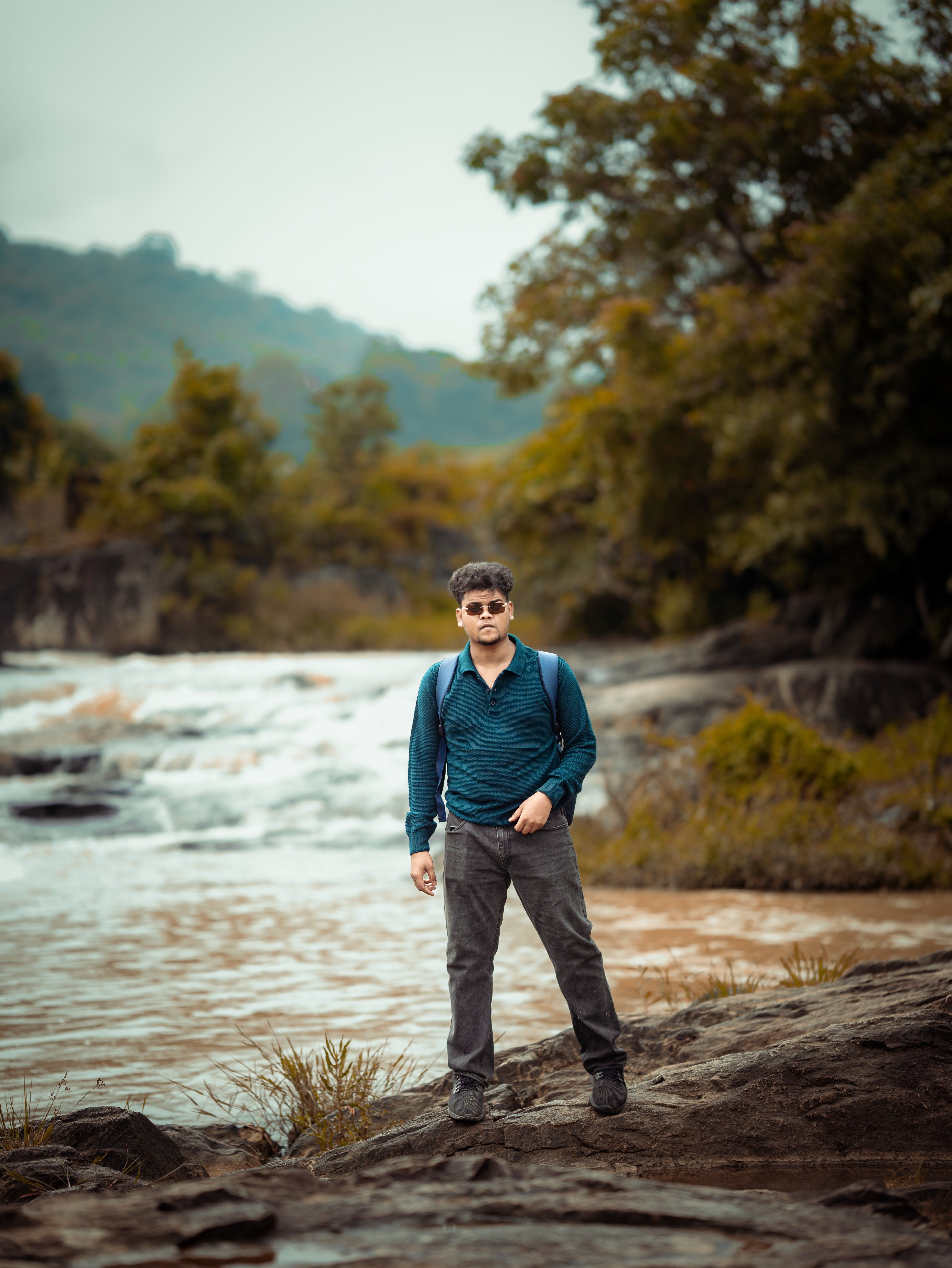 A man stands near a scenic riverbank in Borigumma, India, surrounded by lush greenery.