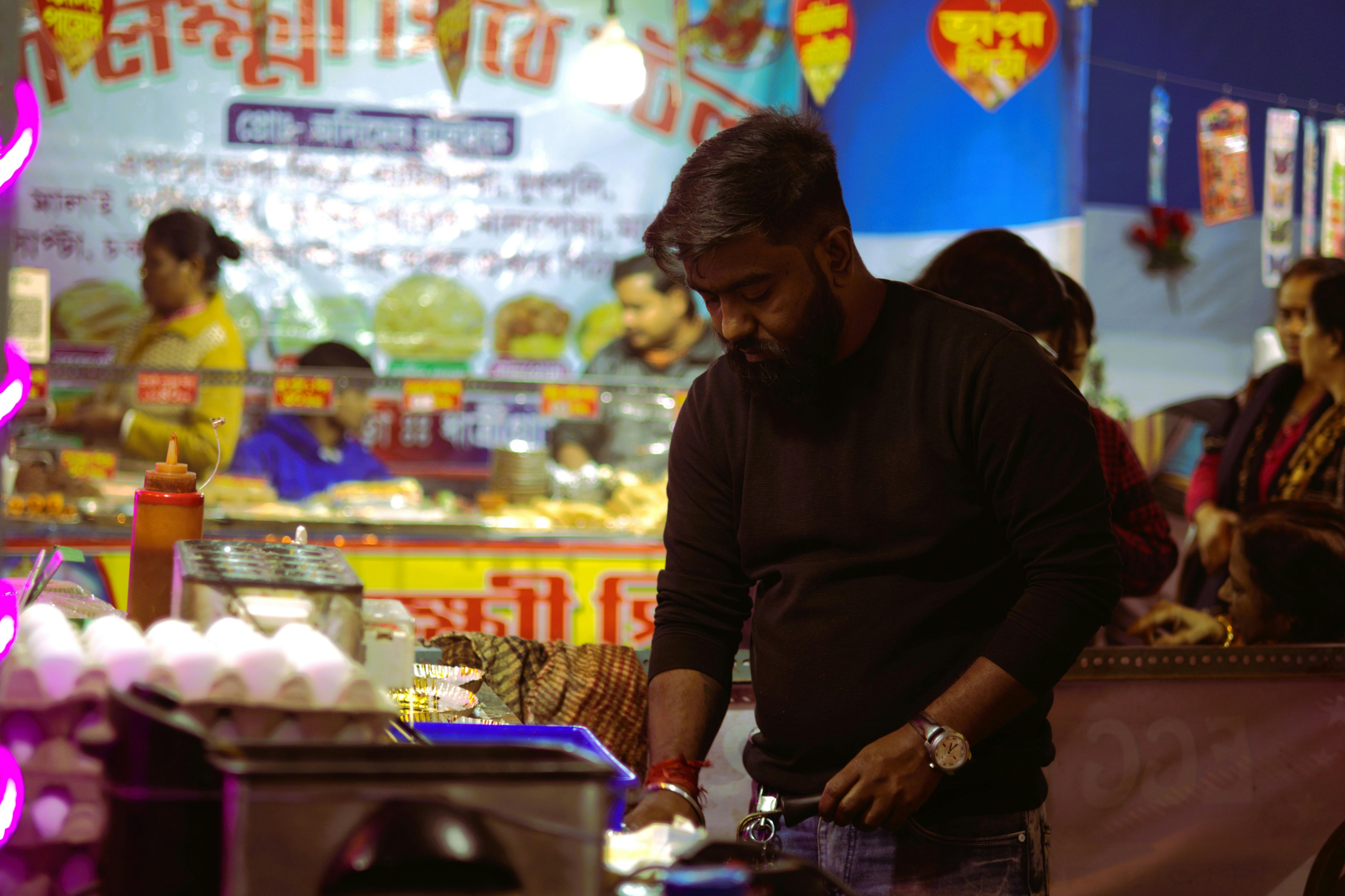 Street food vendor cooking at a vibrant night market with colorful signs and crowd in the background.